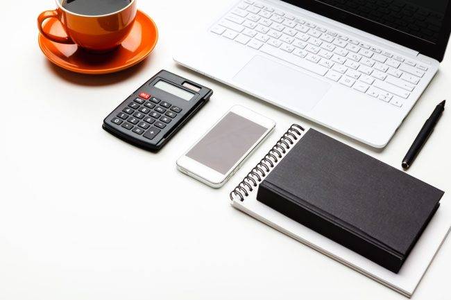 Biurko z laptopem, kalkulatorem, telefonem, notesem i kawą – organizacja pracy w firmie