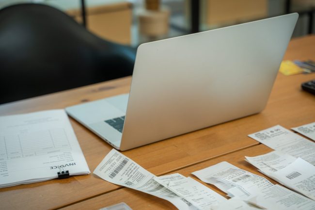 Otwarty laptop na biurku otoczony fakturami i paragonami – księgowość i e-faktury