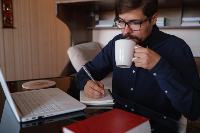 Przedsiębiorca prowadzący jednoosobową działalność pracuje z domu przy laptopie i notatkach