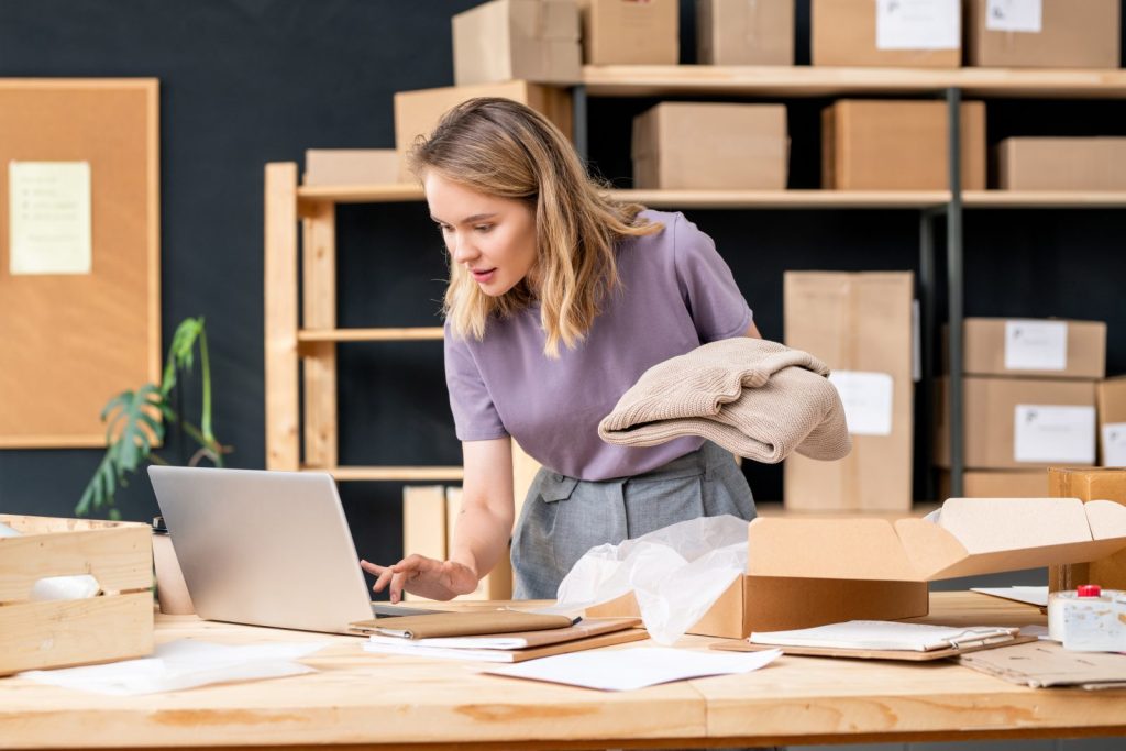 Właścicielka sklepu internetowego pakuje zamówienia przy laptopie – e-commerce