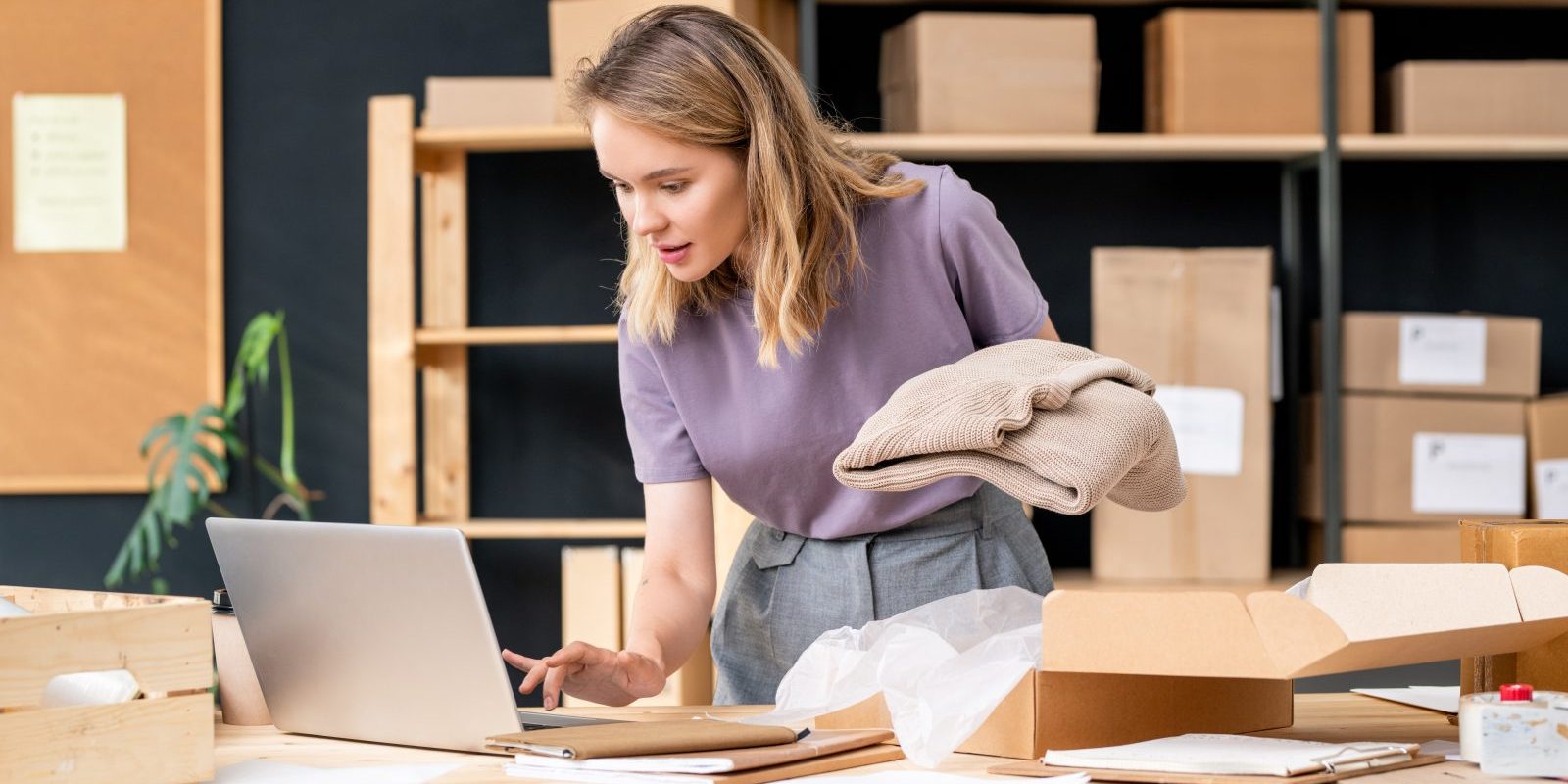 Właścicielka sklepu internetowego pakuje zamówienia przy laptopie – e-commerce