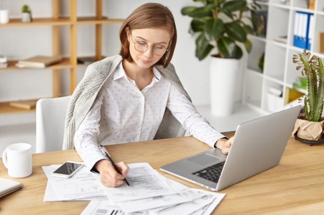 Specjalistka ds. kadr i płac wypełnia dokumenty przy laptopie
