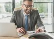 Uśmiechnięty księgowy w garniturze pracuje przy laptopie w biurze