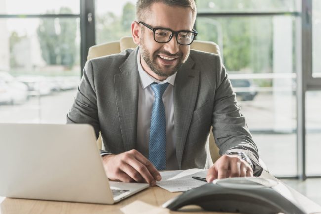 Uśmiechnięty księgowy w garniturze pracuje przy laptopie w biurze